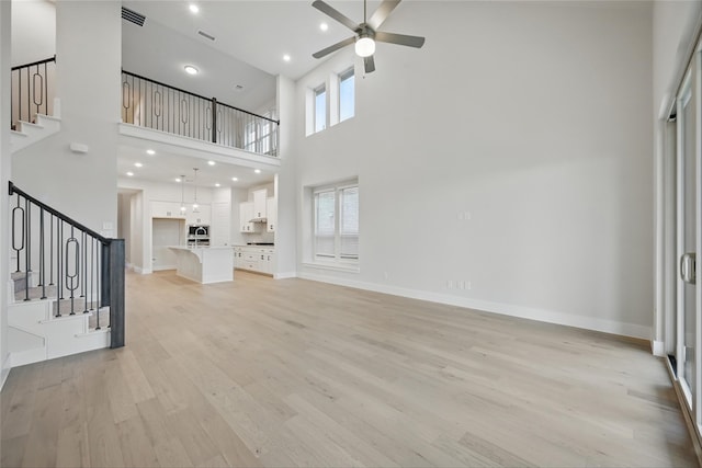 unfurnished living room with ceiling fan, a towering ceiling, stairs, and light wood finished floors