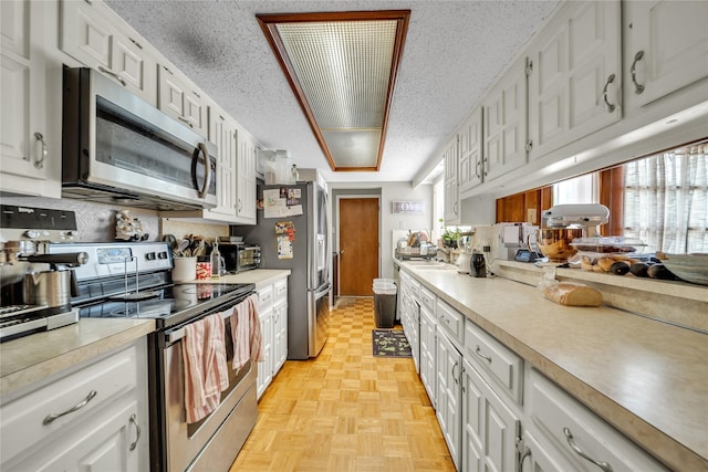 kitchen featuring a textured ceiling, white cabinetry, light countertops, and appliances with stainless steel finishes
