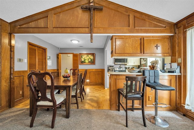 kitchen featuring appliances with stainless steel finishes, wood walls, brown cabinets, and lofted ceiling