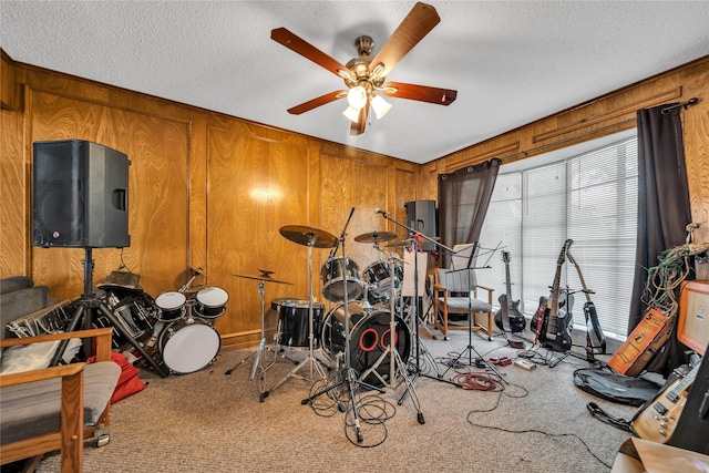recreation room featuring a textured ceiling, wood walls, ceiling fan, and carpet floors