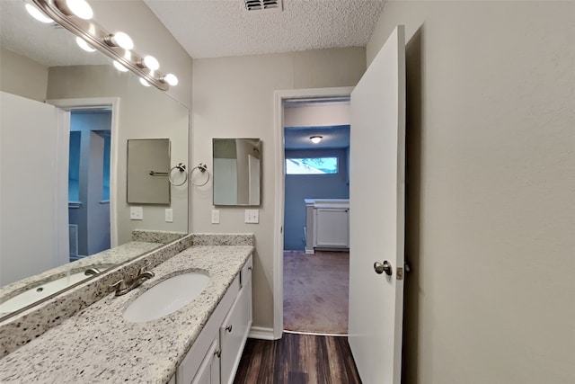 bathroom with a textured ceiling, baseboards, visible vents, vanity, and wood finished floors