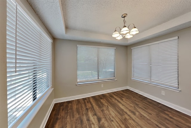 empty room featuring a tray ceiling, a chandelier, a textured ceiling, and dark wood-type flooring