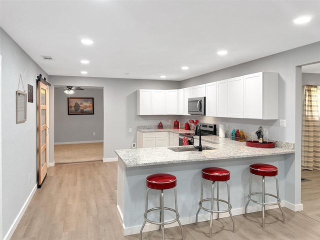 kitchen featuring a peninsula, light wood-type flooring, light stone counters, and appliances with stainless steel finishes