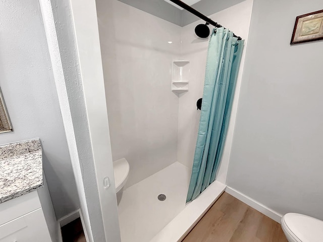 bathroom with toilet, wood finished floors, vanity, and a stall shower