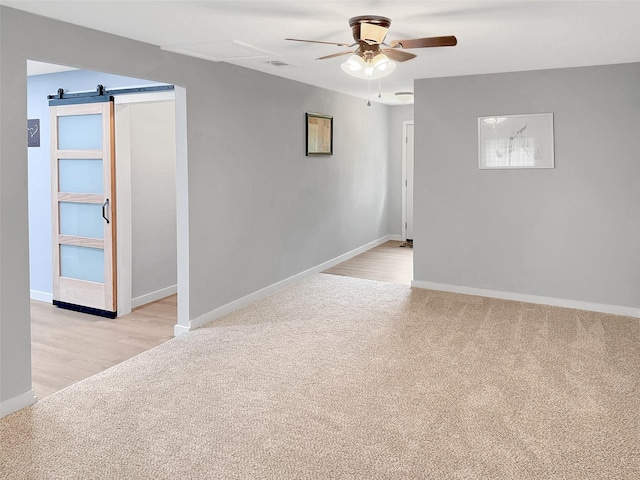 unfurnished room featuring light colored carpet, a barn door, baseboards, and ceiling fan
