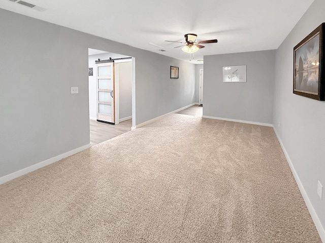 spare room with light colored carpet, a barn door, visible vents, a ceiling fan, and baseboards