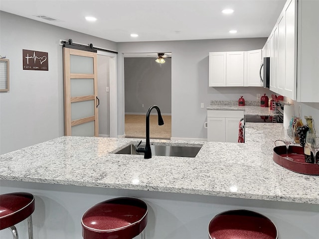 kitchen featuring a barn door, a breakfast bar, light stone counters, a sink, and stainless steel microwave