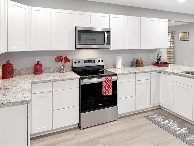kitchen featuring light stone counters, stainless steel appliances, white cabinets, and light wood-style flooring