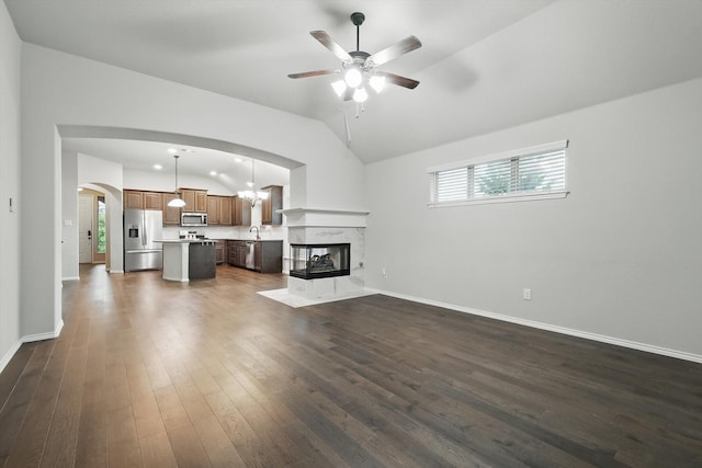 unfurnished living room with lofted ceiling, dark wood-type flooring, arched walkways, a ceiling fan, and baseboards