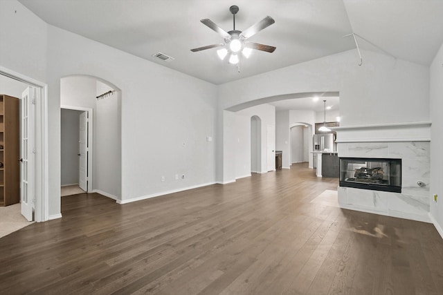 unfurnished living room with lofted ceiling, a premium fireplace, ceiling fan, wood finished floors, and arched walkways