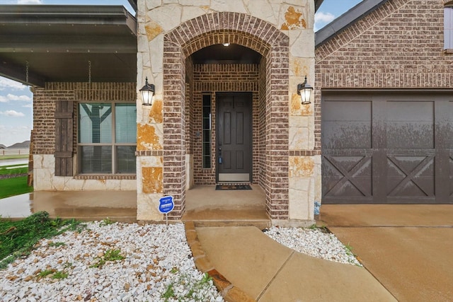 view of exterior entry featuring concrete driveway, stone siding, brick siding, and a garage