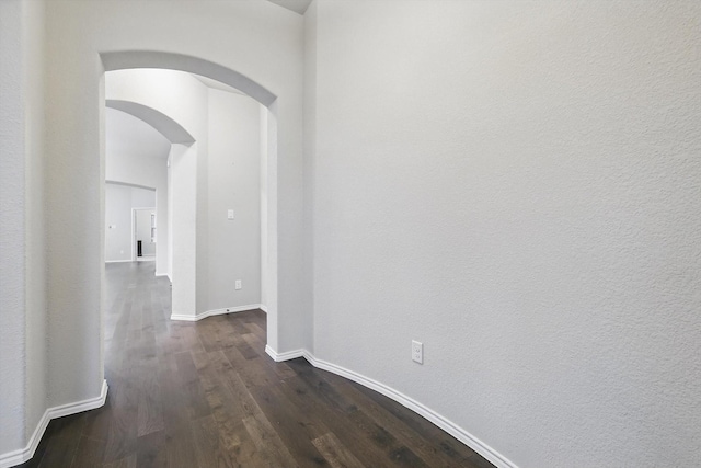corridor with dark wood finished floors, baseboards, and arched walkways