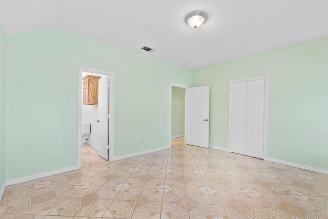 908 E Belknap St, Ennis, TX 75119 - unfurnished bedroom with baseboards, a closet, lofted ceiling, ensuite bath, and light tile patterned flooring