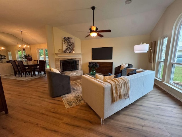living room featuring lofted ceiling, a fireplace, ceiling fan with notable chandelier, and wood finished floors