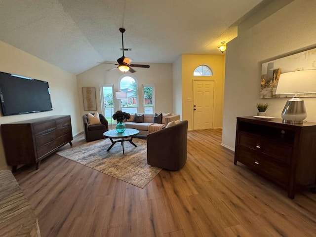 living area with vaulted ceiling, a textured ceiling, a ceiling fan, and wood finished floors
