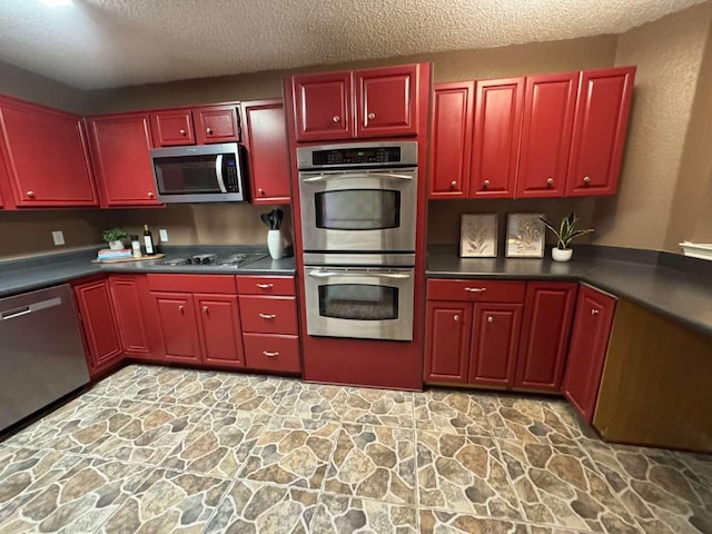kitchen featuring stone floors, a textured ceiling, dark countertops, and appliances with stainless steel finishes