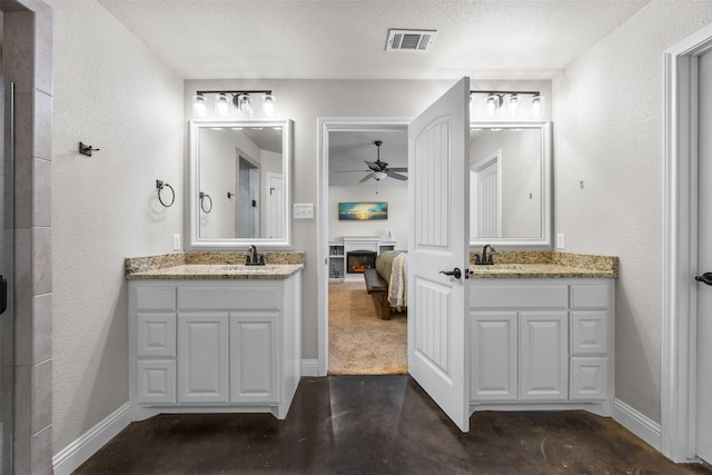 ensuite bathroom with a sink, a warm lit fireplace, visible vents, ceiling fan, and connected bathroom