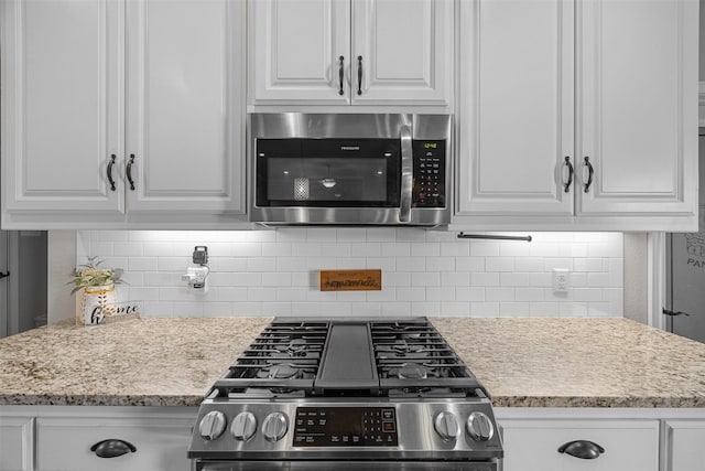 kitchen with appliances with stainless steel finishes, decorative backsplash, light stone countertops, and white cabinetry