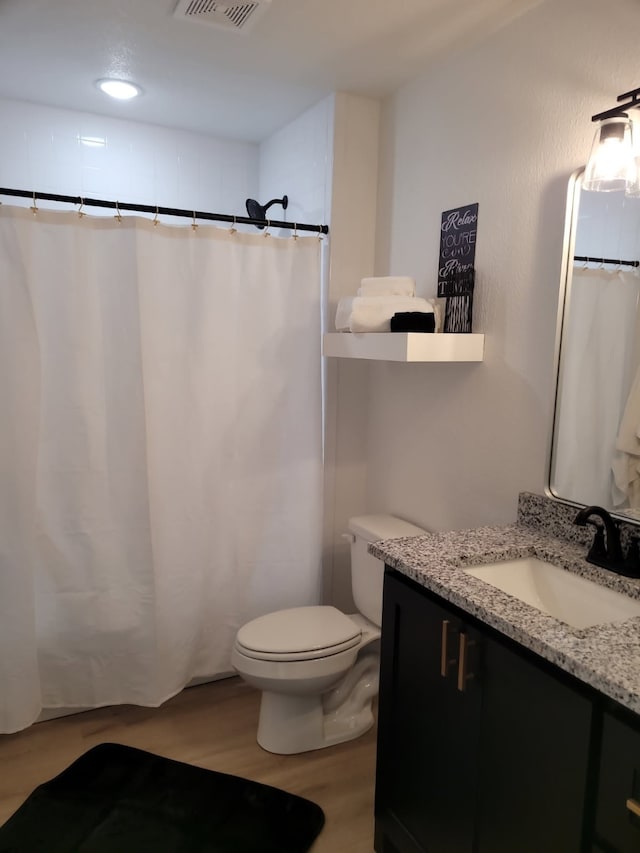 bathroom featuring toilet, wood finished floors, vanity, curtained shower, and visible vents