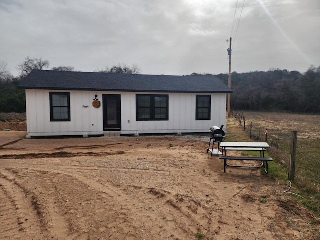view of front of house with board and batten siding, roof with shingles, and fence