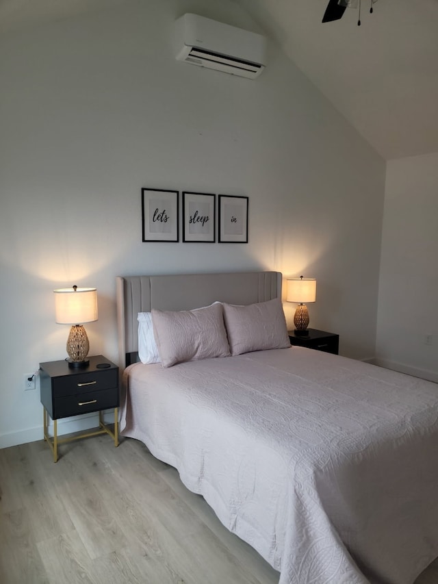 bedroom featuring a wall mounted air conditioner, light wood-type flooring, baseboards, ceiling fan, and lofted ceiling