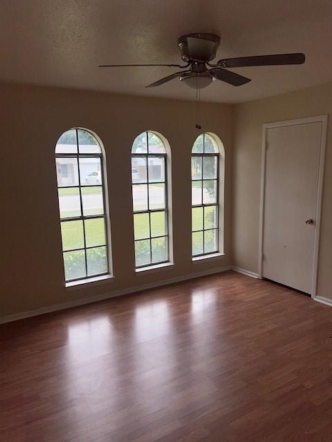 empty room with baseboards, ceiling fan, and wood finished floors