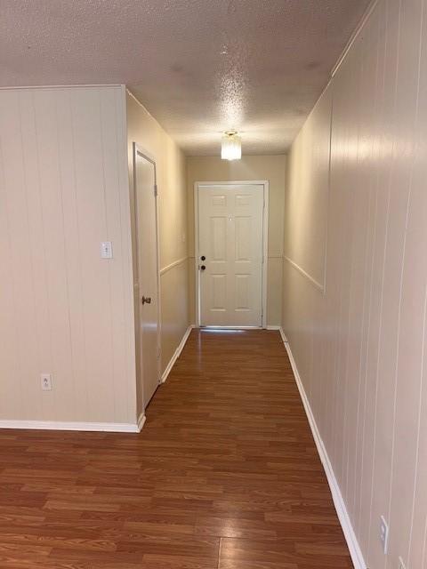 corridor with a textured ceiling, wood finished floors, and baseboards
