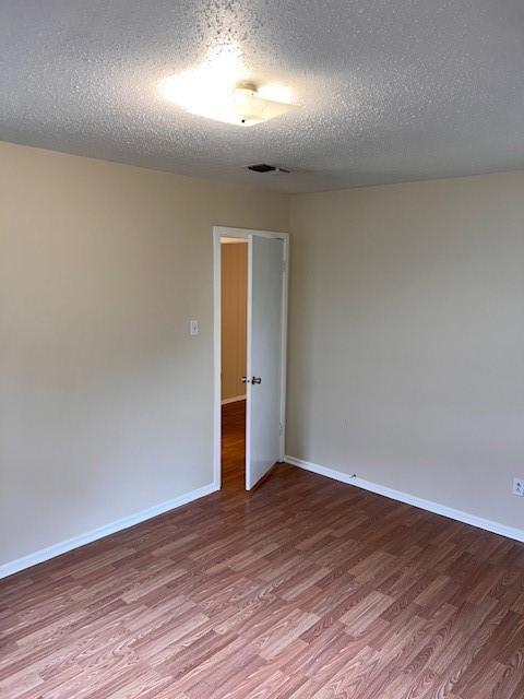 unfurnished room with a textured ceiling, visible vents, wood finished floors, and baseboards