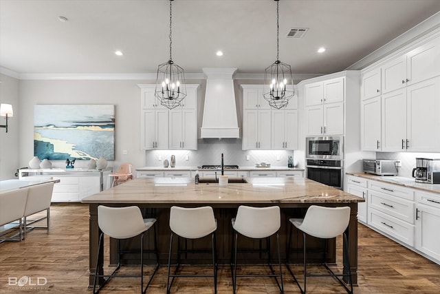 kitchen featuring visible vents, an island with sink, custom exhaust hood, decorative backsplash, and appliances with stainless steel finishes