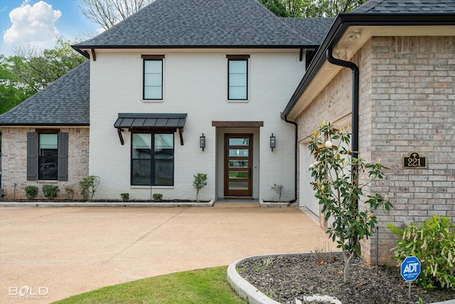 entrance to property featuring brick siding and a shingled roof