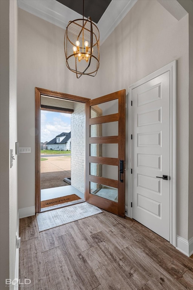 foyer entrance with ornamental molding, a chandelier, a high ceiling, and wood finished floors