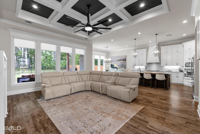 living room featuring ceiling fan with notable chandelier, coffered ceiling, dark wood finished floors, visible vents, and ornamental molding