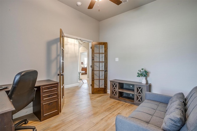 home office with french doors, light wood finished floors, arched walkways, a ceiling fan, and baseboards