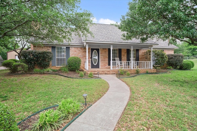 single story home featuring covered porch, a shingled roof, brick siding, and a front yard