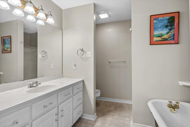 full bath featuring baseboards, toilet, vanity, and a freestanding tub