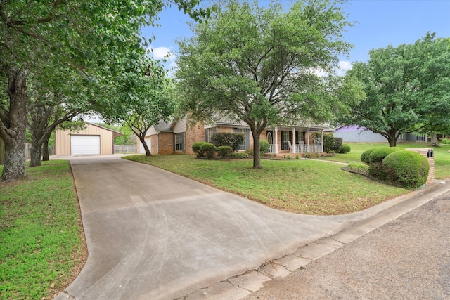 view of property hidden behind natural elements with an outbuilding, brick siding, concrete driveway, a front yard, and a porch