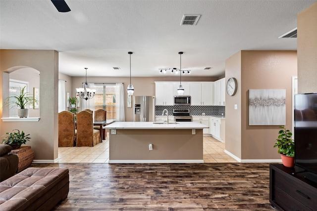 kitchen featuring appliances with stainless steel finishes, open floor plan, arched walkways, white cabinetry, and light wood-type flooring