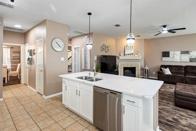 kitchen featuring stainless steel dishwasher, a sink, open floor plan, white cabinetry, and a tile fireplace