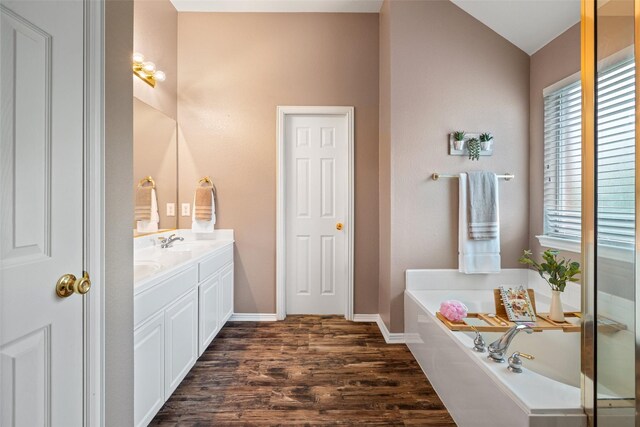 full bath with wood finished floors, vanity, a garden tub, baseboards, and lofted ceiling