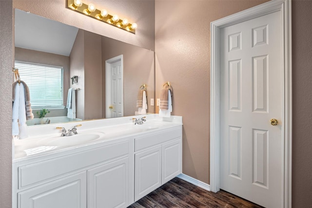 full bathroom with wood finished floors, double vanity, lofted ceiling, baseboards, and a textured wall