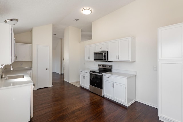 kitchen with a sink, lofted ceiling, dark wood finished floors, light countertops, and appliances with stainless steel finishes