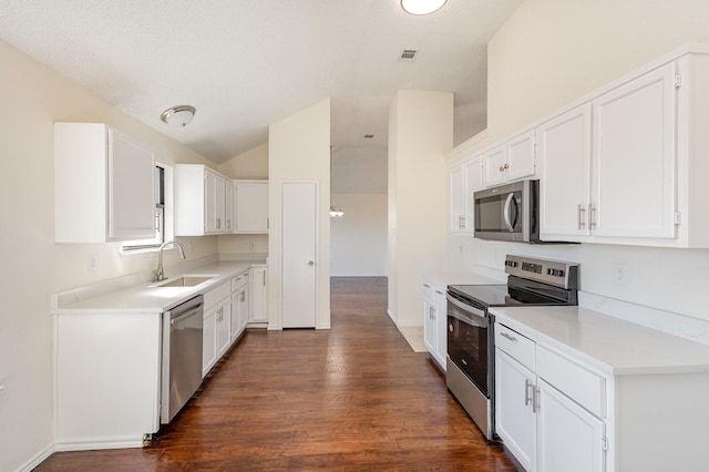 kitchen featuring a sink, stainless steel appliances, vaulted ceiling, dark wood-style flooring, and white cabinetry