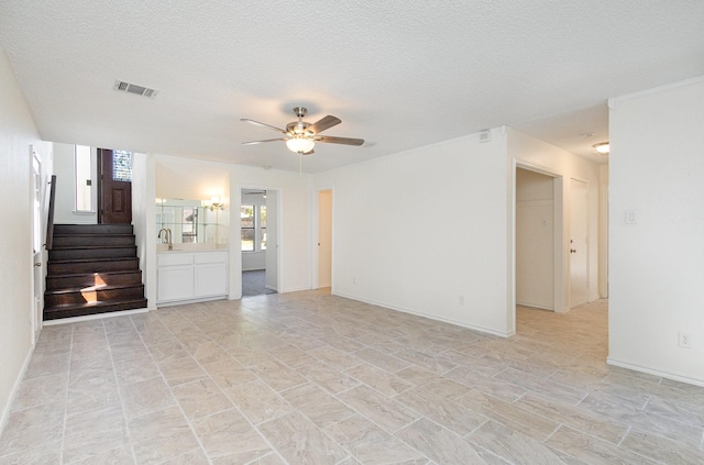 unfurnished living room featuring a ceiling fan, a textured ceiling, visible vents, baseboards, and stairs