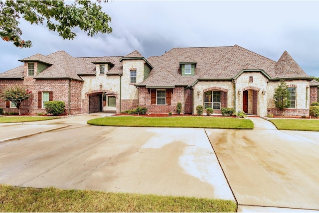 french country home featuring a front lawn, stone siding, brick siding, and curved driveway