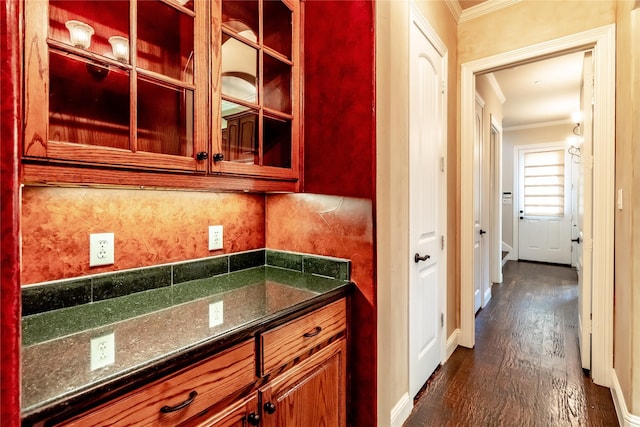 kitchen with dark stone counters, ornamental molding, dark wood-style flooring, decorative backsplash, and glass insert cabinets