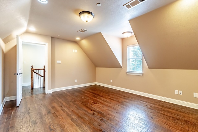 additional living space featuring baseboards, dark wood finished floors, visible vents, and vaulted ceiling
