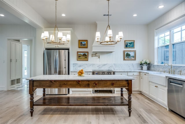 kitchen with a notable chandelier, light stone countertops, light wood finished floors, stainless steel appliances, and white cabinets