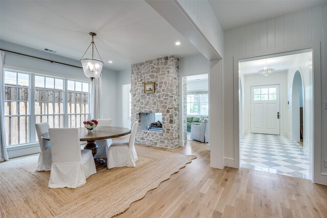 dining area featuring recessed lighting, a stone fireplace, visible vents, arched walkways, and light wood-type flooring