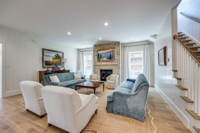 living area featuring stairs, a healthy amount of sunlight, a fireplace, and light wood-type flooring