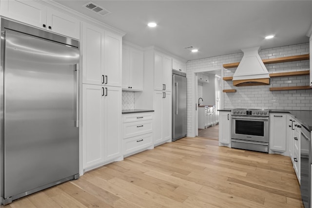 kitchen featuring visible vents, custom range hood, open shelves, dark countertops, and stainless steel appliances